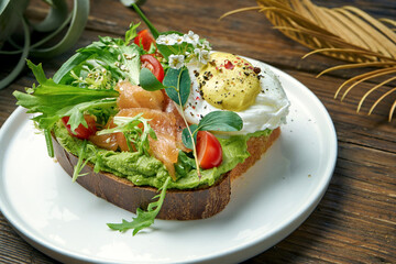 Trend street food - avocado toast with guacamole, poached egg and salmon in a plate on a wooden background
