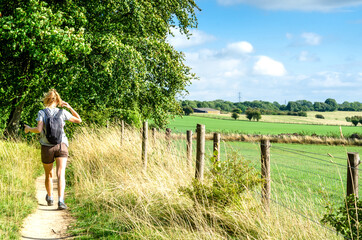 Woman hiking on footpath by agricultural fields. Photo taken on the Cotswold Way in...