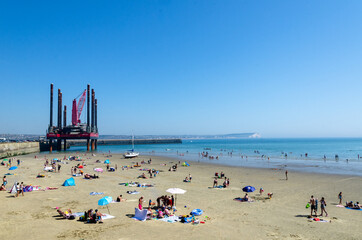 People enjoying the hot weather at Newhaven west beach in East Sussex, England. The iconic Seven Sisters cliffs can be seen in the far background
