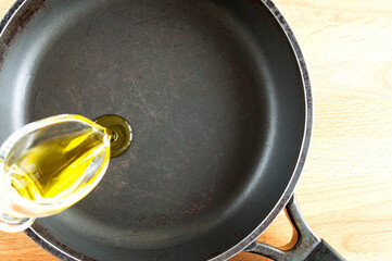 Pouring olive oil to an old cast-iron pan. Tool with cracks and scuffs. Top view, place for text