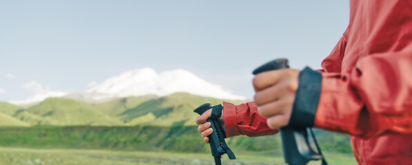 Female hands with trekking poles in front of mountain Elbrus.