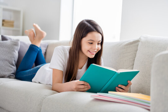 Photo of little pretty pupil school lady lying comfy sofa reading diary book positive good mood diligent student social distance quarantine home study comfort room indoors