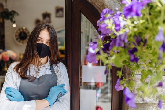 Coronavirus covid 19. Floral shop woman owner in gloves with face mask, open door after lockdown quarantine. Announcement we are open nv doors, flower shops, cafes, local, small businesses concept.