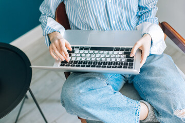 Fototapeta premium Beautiful brunette with a short haircut works in the home office on a blue background. Typing on a laptop, calling on the phone, transferring documents, making notes, drinking coffee from a mug.