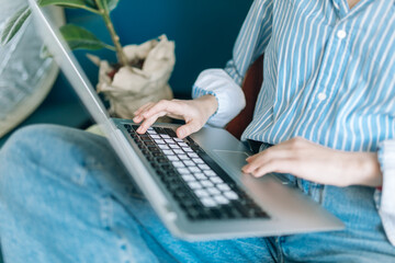 Beautiful brunette with a short haircut works in the home office on a blue background. Typing on a laptop, calling on the phone, transferring documents, making notes, drinking coffee from a mug.