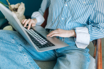 Beautiful brunette with a short haircut works in the home office on a blue background. Typing on a laptop, calling on the phone, transferring documents, making notes, drinking coffee from a mug.