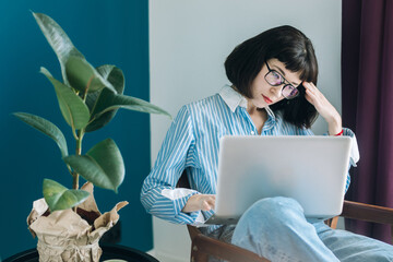 Beautiful brunette with a short haircut works in the home office on a blue background. Typing on a laptop, calling on the phone, transferring documents, making notes, drinking coffee from a mug.