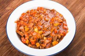 Veal stewed with vegetables in tomato sauce on a board background.