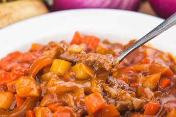 Veal stewed with vegetables in tomato sauce on a board background.