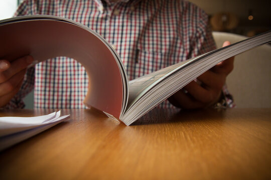 Open book in front of a checkered shirt on a wooden table, horizontal layout.