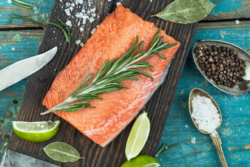 A piece of raw salmon, spices, knife, board, spoon, lime on an old worn desk, top view, close-up. Preparation for cooking fish food. Salmon steak.