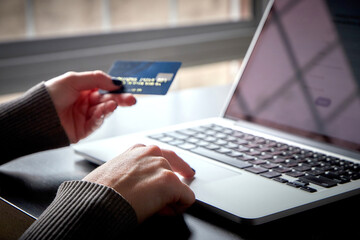 Close-up of Caucasian woman's hands with blue nails, holding credit card while purchasing online on her laptop