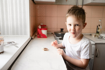 a little boy sits at the kitchen table looks slyly into the camera, eats bread with chocolate paste, morning breakfast