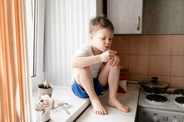 little boy sits on the kitchen table eats bread with chocolate paste, morning excerpts on the windowsills, cute baby