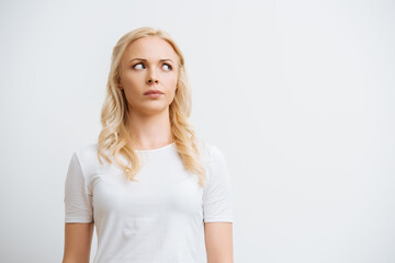 thoughtful blonde woman looking away while standing isolated on white