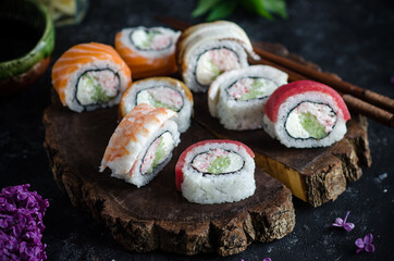 Different sushi rolls with with shrimp, tuna and red fish, wasabi and ginger on a plate on wooden background. Top view. Bouquet of lilacs on the table.