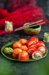 Different sushi rolls with red caviar and salmonl, wasabi and ginger on a plate on wooden background.