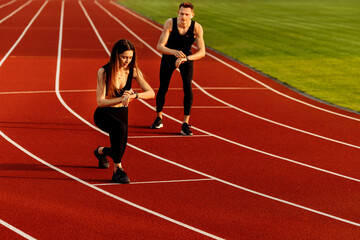 Beautiful sporty woman and young sporty man are ready to run on racetrack. 