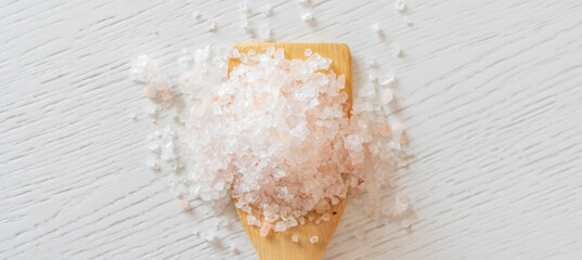 a wooden spoon with sea salt on the table, top view isolated