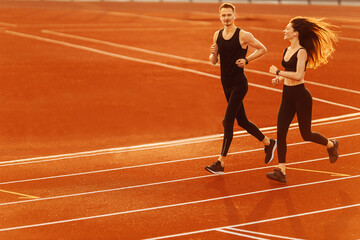 Young man and woman running on race track in modern stadium. 