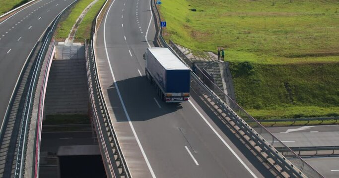 Truck rides on bridge and continues to move along road. Truck rides along bridge, from below passes road along which other trucks go. Aerial view.