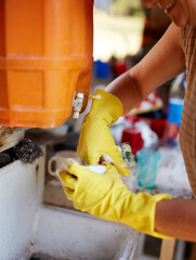 Woman with gloves washing dishes in a retro sink with a camping water tank.