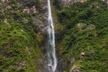 Fototapeta na wymiar Stunning landscape of waterfall, lush green & rocky mountains and clouds. Monsoon trek to Ghangaria taken in August starts near Govindghat in Uttarakhand India.
