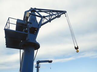 Blue harbor crane with suspended hook and white cloudy sky. Heavy load dockside cranes in port,...
