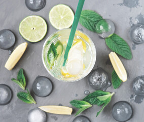 Ingredients for making mojito on grey background. lime, lemon, mint leaves and high glass with ice cubes. summer non-alcoholic cocktail. top view, flat lay