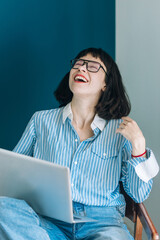 Beautiful brunette with a short haircut works in the home office on a blue background. Typing on a laptop, calling on the phone, transferring documents, making notes, drinking coffee from a mug.