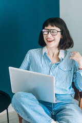 Beautiful brunette with a short haircut works in the home office on a blue background. Typing on a laptop, calling on the phone, transferring documents, making notes, drinking coffee from a mug.