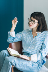 Beautiful brunette with a short haircut works in the home office on a blue background. Typing on a laptop, calling on the phone, transferring documents, making notes, drinking coffee from a mug.