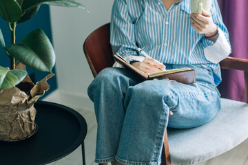Beautiful brunette with a short haircut works in the home office on a blue background. Typing on a laptop, calling on the phone, transferring documents, making notes, drinking coffee from a mug.