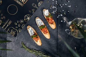 Italian cuisine, antipasti and tapas. Bruschetta of baguette and cottage cheese, tomato, salmon capers, pesto. Serving dishes in a restaurant in white plate.