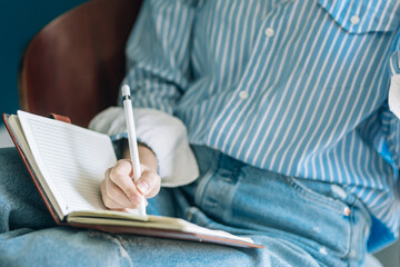 Beautiful brunette with a short haircut works in the home office on a blue background. Typing on a laptop, calling on the phone, transferring documents, making notes, drinking coffee from a mug.