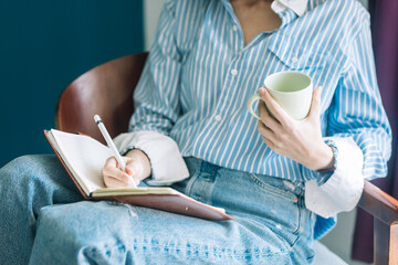 Beautiful brunette with a short haircut works in the home office on a blue background. Typing on a laptop, calling on the phone, transferring documents, making notes, drinking coffee from a mug.
