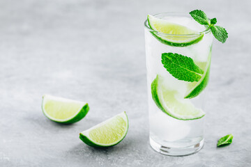 Mojito cocktail with ice, fresh mint and lime in glass on gray stone background.