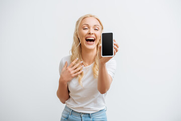 excited girl laughing while showing smartphone with blank screen isolated on white