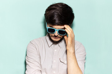 Portrait of young sad guy wearing shades on background of aqua menthe color.