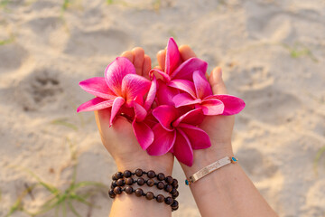 person holds exotic frangipani flowers in his hands, a golden bracelet with topazes, the word 