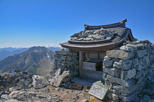 剱岳山頂のお宮と立山。北アルプス立山連峰の剱岳（つるぎだけ、標高2,999m）の頂上に鎮座するお宮と、立山連峰主峰、立山三山、雄山（おやま、標高3003 m）、大汝山（おおなんじやま3015 m）、富士ノ折立（ふじのおりたて2999 m）小さく劔沢小屋。The mountaintop of Mt.Tsurugidake. in the nothernalps and Tateyama range.