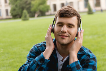 happy student with closed eyes touching wireless headphones and listening music