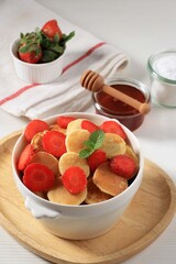 Bowl with Tiny Pancake Cereal with Strawberries and Mint Leaves on a WhiteBackground. and Wooden Plate. Trendy food. Mini cereal pancakes. Portrait Orientation
