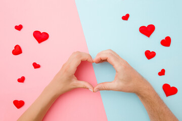 Heart shape created from young woman and man hands on light pink blue table background. Red small...