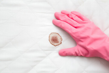 Hand in rubber protective glove showing on mattress blood stain after night menstruation. Fresh or...