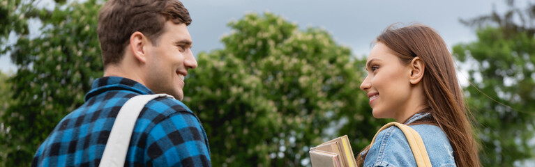 panoramic crop of happy and young woman holding books and looking at handsome student