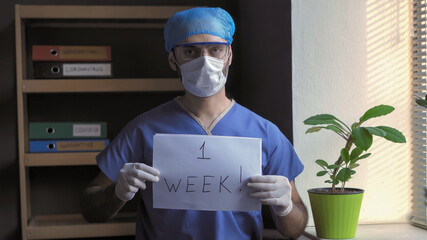Doctor announces the end of quarantine. Man in protective uniform shows message 1 week standing in...