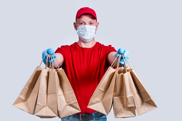 Safe delivery. A courier in a red uniform and protective mask and gloves holds a large order, many paper bags, contactless delivery food in quarantine. Donation of volunteers. Zero waste