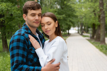 Fototapeta premium handsome boyfriend and pretty girlfriend with closed eyes hugging in park
