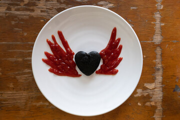 Heart chocolate cake have decorated by ketchup is drawing wings on white plate. for kid meal.